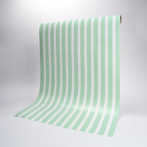 May include: A roll of green and white striped wallpaper. The wallpaper is unrolled and curved, showing the pattern.