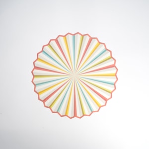 May include: A colorful, circular design with radiating stripes in shades of pink, yellow, blue, and green. The design has a starburst effect, creating a sense of movement and energy.
