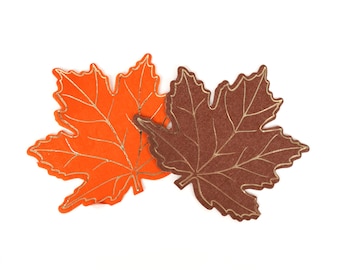 May include: Two paper maple leaves, one orange and one brown, with gold foil accents. The leaves are overlapping and are on a white background.