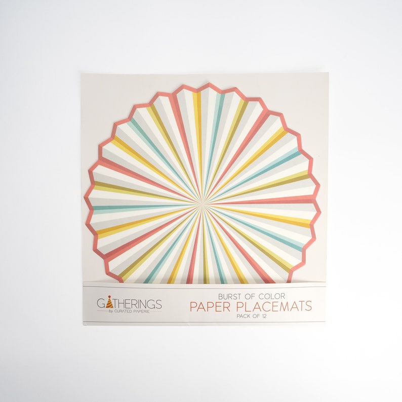 May include: A pack of 12 paper placemats with a burst of color design. The placemats are round and have a radial pattern of pink, yellow, and blue stripes. The text "BURST OF COLOR PAPER PLACEMATS PACK OF 12" is printed on the packaging.