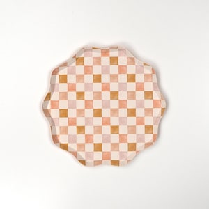 May include: A round, scalloped-edge paper plate with a checkered pattern in shades of pink and brown.