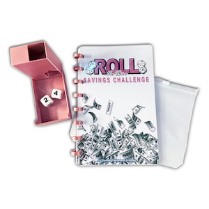 May include: A pink dice box with two white dice showing the numbers 2 and 4. A spiral-bound notebook with the text "Roll the Dice Savings Challenge" and illustrations of money. A clear plastic pouch is also included.