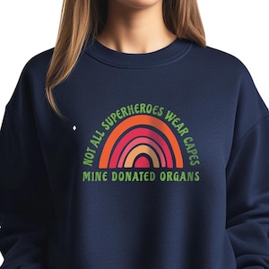 May include: A navy blue sweatshirt with a rainbow graphic and the text "Not all superheroes wear capes. Mine donated organs."