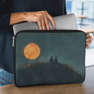 May include: A dark blue laptop sleeve featuring a design of two silhouettes of people sitting on a hill beneath a large orange moon. The moon is surrounded by a white glow.