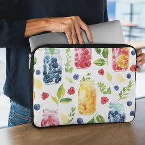 May include: A white laptop sleeve featuring a colourful watercolour pattern of mason jars filled with blueberries, raspberries, lemons, and oranges. The jars are surrounded by green leaves and small berries.