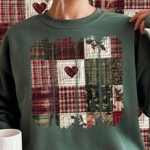 May include: A dark green sweatshirt featuring a patchwork design with red, white, and green plaid and floral patterns. The design includes a heart shape and the text "SMALL TOWN". The sweatshirt is a comfortable, casual style.