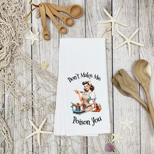 May include: White kitchen towel with a vintage illustration of a woman cooking. The text on the towel reads "Don't Make Me Poison You".