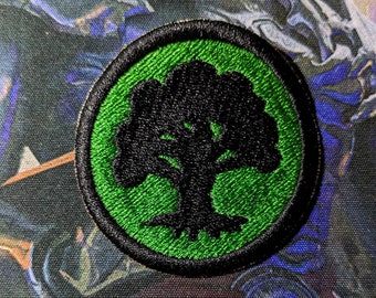 May include: A green and black embroidered patch with a tree design. The tree is black and the background is green.