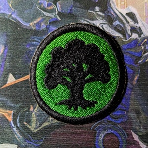 May include: A green and black embroidered patch with a tree design. The tree is black and the background is green.