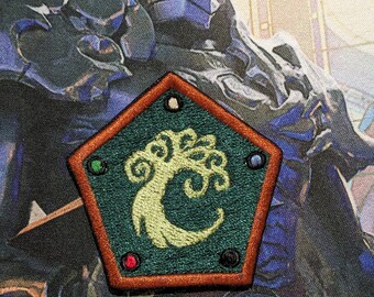 May include: A green and brown embroidered patch with a stylized tree design and four colored dots around the edge. The patch is shaped like a pentagon.