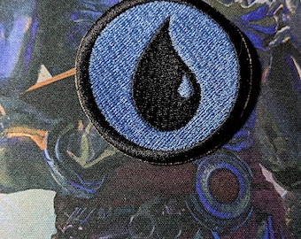May include: A blue and black embroidered patch with a teardrop shape. The patch is circular and has a black border.