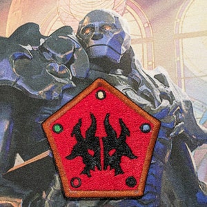 May include: A red, pentagon-shaped patch with a black, stylized creature with horns and glowing eyes in the center. The patch has a brown border and four small, colored circles around the creature.