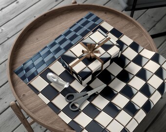 May include: A wrapped gift box with a brown ribbon sits on a wooden table, next to wrapping paper and scissors. The gift box and wrapping paper feature a black, white, and blue geometric pattern. A roll of blue patterned wrapping paper and a silver tape dispenser are also present.