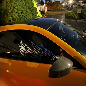 Puede incluir: Un coche amarillo con techo negro y un espejo lateral de fibra de carbono. El coche tiene una calcomanía de llama en la ventana.