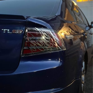 May include: A dark blue car with a rear taillight that has a custom flame design. The car has a "TL TYPE S" badge on the back.