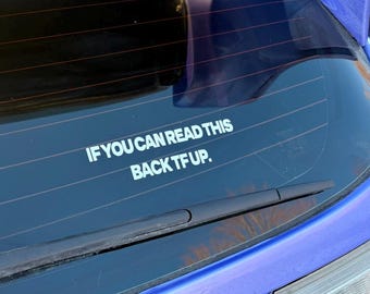 May include: A white decal on a car's rear window with the text "IF YOU CAN READ THIS BACK TF UP." The decal is centered below the rear window wiper. The car is a vibrant blue.