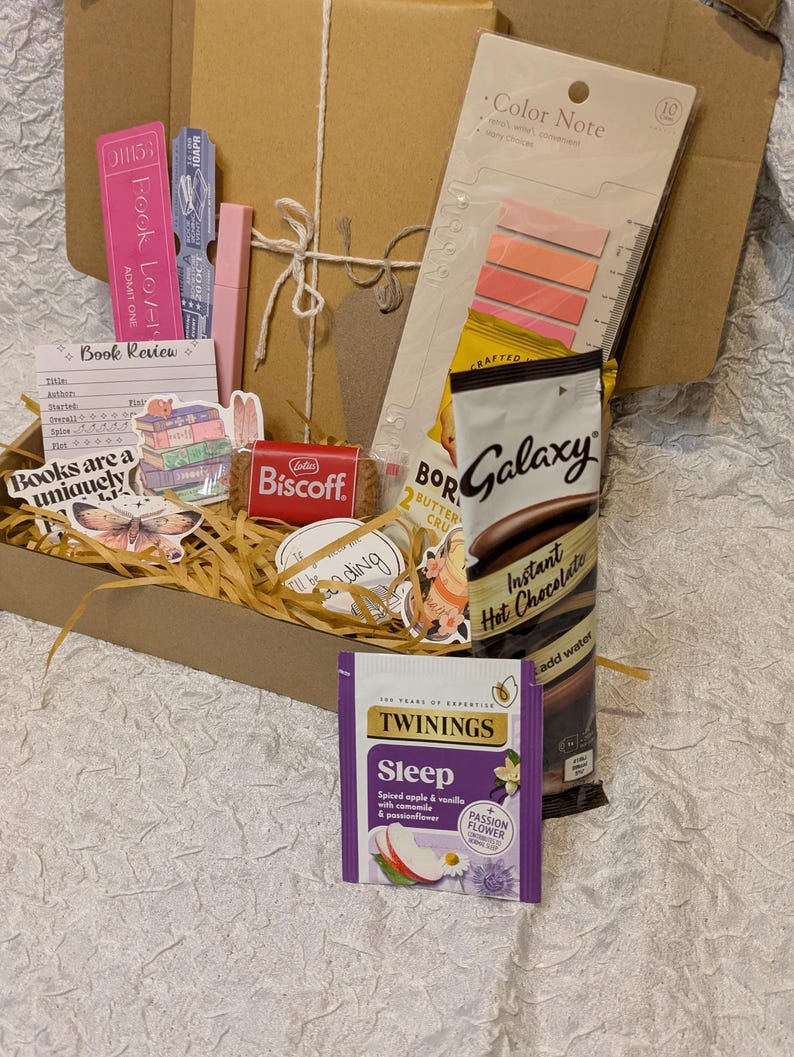 May include: A brown cardboard box filled with various items, including bookmarks, stickers, a Lotus Biscoff cookie, and a packet of Galaxy Instant Hot Chocolate. The box also contains a packet of Twinings Sleep tea and a Color Note sticky note pad.