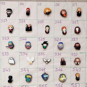 May include: A selection of colourful, miniature character charms, possibly for shoes or accessories. The charms depict various figures, including a wizard, a ghost, and a lightning bolt. The charms are arranged on a white surface.