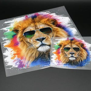 Könnte beinhalten: Ein Löwe mit Sonnenbrille vor einem bunten Aquarellhintergrund. Der Löwe schaut direkt in die Kamera.