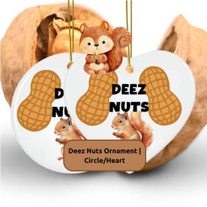 May include: Two white ceramic Christmas decorations, one round and one heart-shaped, with a peanut design and the text "Deez Nuts". Each decoration features a cartoon squirrel holding a peanut.