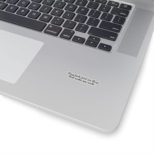 Op de afbeelding: Een sticker met de tekst "Tiny task: find one thing that makes you smile" in een handgeschreven lettertype. De sticker bevindt zich op een zilveren laptop, in de buurt van het toetsenbord.