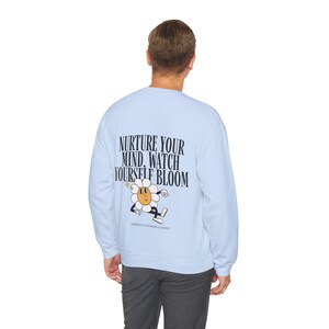 May include: A light blue sweatshirt with a cartoon flower graphic and the text "Nurture your mind, watch yourself bloom. Embrace your mindful habits."