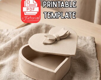 May include: A heart-shaped box with a lid, featuring a bow detail, is open on a wooden surface. The box is a neutral beige color. The text "PRINTABLE TEMPLATE" is displayed in black capital letters.