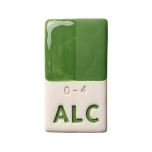 May include: A rectangular ceramic tile with a two-tone green glaze over a white base. The top half is glossy, the bottom half is matte. The base has the text "0-4" and "ALC" in a green font. The tile is a sample for pottery.