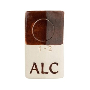 May include: A rectangular ceramic tile with a two-tone brown glaze. The top half is divided, with a circle in the center. The bottom half is off-white with the letters "ALC" and the numbers "1-2" etched into the surface.