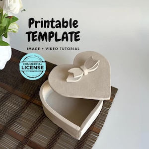 May include: A printable template for a heart-shaped box with a bow on the lid. The template is for a craft project and includes a commercial license. The image shows the box open, revealing the inside.
