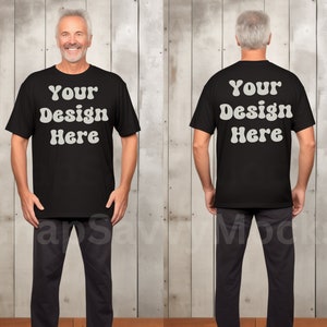 Könnte beinhalten: Ein schwarzes T-Shirt-Mockup mit dem Text "Your Design Here" auf der Vorder- und Rückseite. Das Shirt wird von einer Person getragen, die vor einem Hintergrund aus Holzpaneelen steht.