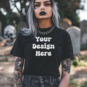 Peut inclure: Un t-shirt noir avec le texte "Your Design Here" en blanc, porté par une personne aux cheveux argentés et des tatouages. La personne est debout devant un fond de pierre.