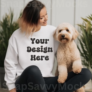 May include: A white sweatshirt with the text "Your Design Here" in black, retro-style lettering. A woman is wearing the sweatshirt and sitting with a small, light brown dog.