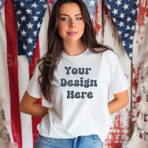 May include: A white t-shirt with the text "Your Design Here" in a retro font. The shirt is being modeled by a person with long brown hair. The background is a red, white, and blue American flag.