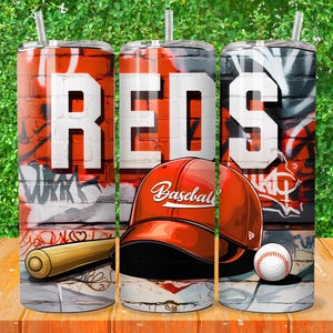 Pode incluir: Três copos de aço inoxidável com um design de grafite vermelho, branco e preto. Os copos apresentam a palavra "REDS" em letras brancas e um boné de beisebol com a palavra "Baseball" nele. Os copos estão sobre uma superfície de madeira.