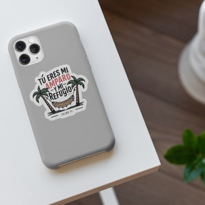 Peut inclure: Une coque de t&eacute;l&eacute;phone grise avec un autocollant blanc repr&eacute;sentant un hamac entre deux palmiers. L'autocollant dit "T&Uacute; ERES MI AMPARO Y MI REFUGIO" et "SALMO 91".