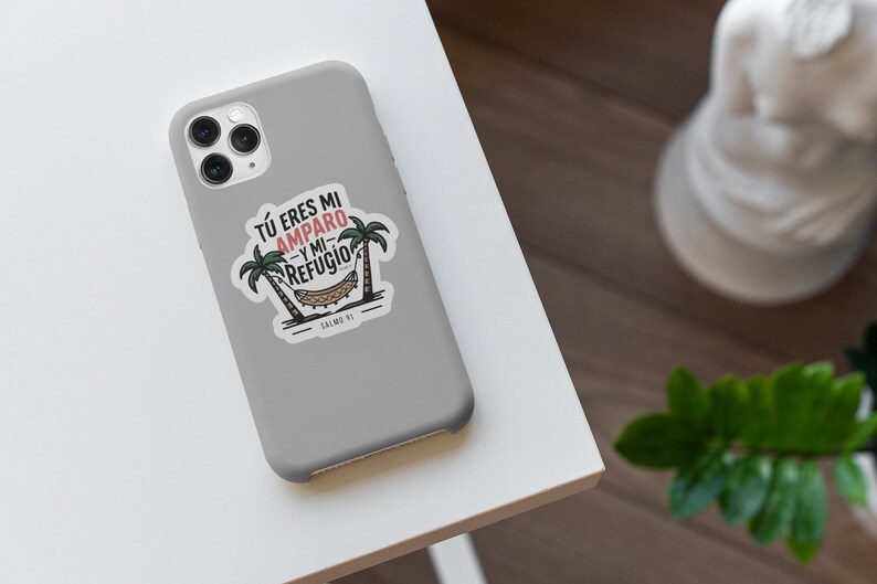 Peut inclure: Une coque de t&eacute;l&eacute;phone grise avec un autocollant blanc repr&eacute;sentant un hamac entre deux palmiers. L'autocollant dit "T&Uacute; ERES MI AMPARO Y MI REFUGIO" et "SALMO 91".