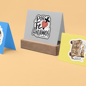 Peut inclure: Trois cartes de v&oelig;ux avec des citations religieuses et des illustrations. La premi&egrave;re carte est bleue et repr&eacute;sente un escalier avec le texte "Yo Camino con Dios". La deuxi&egrave;me carte est grise et repr&eacute;sente un c&oelig;ur avec une croix et le texte "Por Fe Andamos 2 Corintios 5:7". La troisi&egrave;me carte est jaune et repr&eacute;sente une bougie avec le texte "Deja Brillar Tu Luz Mateo 5:16".