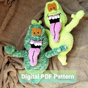 May include: Two green crocheted ghost plushies with pink tongues and white teeth. The ghosts are sitting on a brown fabric background. The text "Digital PDF Pattern" is displayed below the ghosts.
