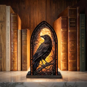 Könnte beinhalten: Dekorative Rabenlampe mit Buntglaseffekt. Der schwarze Rabe sitzt auf einem Ast in einem bogenförmigen Rahmen mit warmem, leuchtendem Hintergrund. Die Lampe steht vor einer Kulisse aus antiken Büchern.