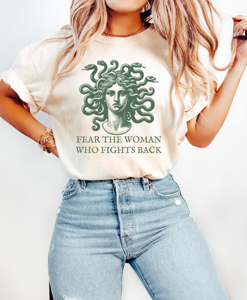 May include: A white t-shirt with a green illustration of Medusa, a mythical Greek figure with snakes for hair. The text "Fear the woman who fights back" is printed below the illustration.