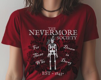 May include: A dark red t-shirt with the words "THE NEVERMORE SOCIETY" and a skeleton in a top hat. The design includes the phrases "For Those Who Dream in Decay" and "EST - 1843" with a rose background.