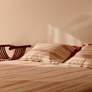 May include: A striped bedspread with two matching pillows on a bed. A wooden chair with arms is mounted on the wall behind the bed.