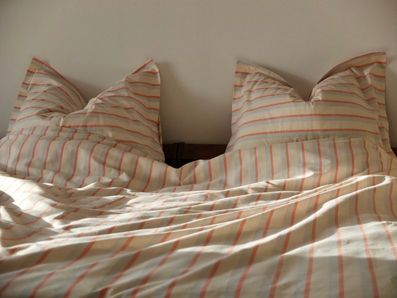 Puede incluir: Un juego de cama a rayas blancas y naranja claro con dos almohadas a juego. La ropa de cama est&aacute; hecha de una tela suave y c&oacute;moda y tiene un aspecto relajado y casual.