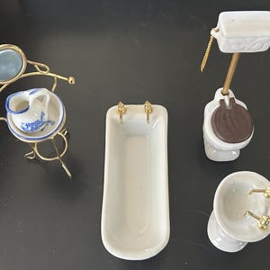 May include: Miniature porcelain bathroom set including a bathtub, sink, toilet, and a wash basin with a mirror. The set features gold-colored metal accents and blue and white details.