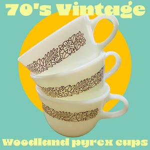 May include: Three vintage 70's Pyrex cups with a woodland floral design in brown on a white background. The cups are stacked on top of each other.