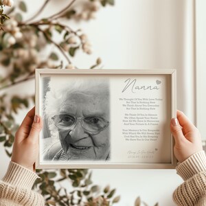 May include: A framed black and white photograph and poem. The photograph features an elderly woman wearing glasses. The poem is dedicated to "Nanna" and includes the dates 25.06.95-22.01.23. The frame is a light beige colour.
