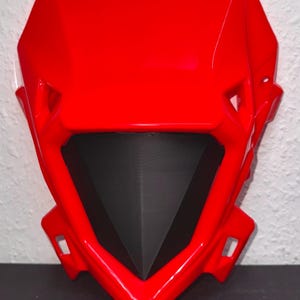 May include: A bright red motorcycle fairing with a black center section. The fairing has a glossy finish and a streamlined design, featuring angular shapes and mounting points.