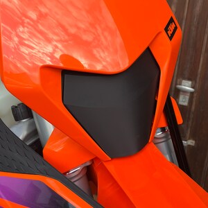 May include: Close-up of an orange motorcycle headlight with a black visor and the KTM logo on the side.