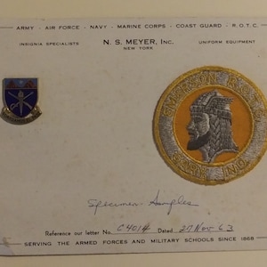 May include: A white card with the text "ARMY - AIR FORCE - NAVY - MARINE CORPS - COAST GUARD - R.O.T.C. INSIGNIA SPECIALISTS N.S. MEYER, INC. NEW YORK UNIFORM EQUIPMENT" printed on it. There are two patches on the card. One is a blue and gold patch with the text "GUARDANDO EL PASO" and a crossed sword and rifle. The other is a yellow and gold patch with the text "EMERSON ROOSEVELT GARP INDO". The text "Specimen Samples Reference our letter No. C4014 Dated 27 Nov 63 SERVING THE ARMED FORCES AND MILITARY SCHOOLS SINCE 1868" is handwritten on the card.